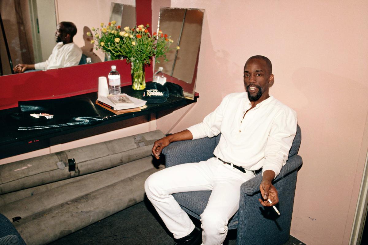 Man wearing an all white outfit sitting in a chair holding a cigarette.